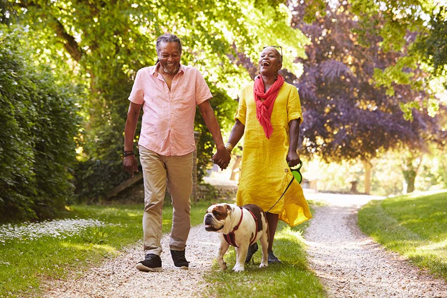 A man and woman smile while walking a dog on an outdoor path