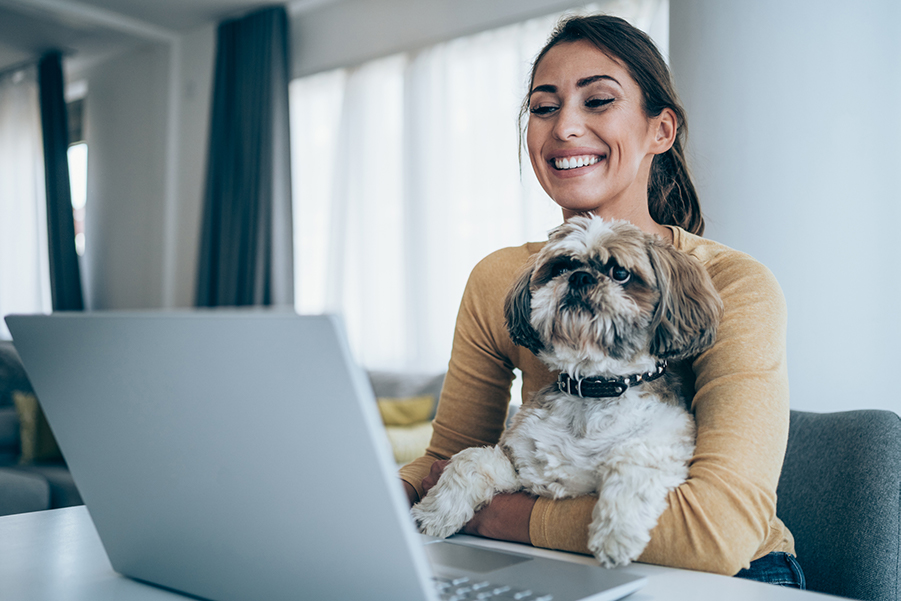 Woman on computer with her dog in her hand.