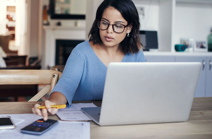 Woman uses calculator while working on a computer