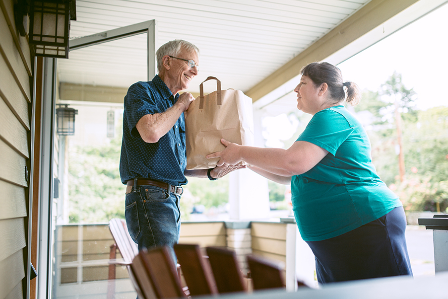 Woman delivering groceries to an older gentleman. 