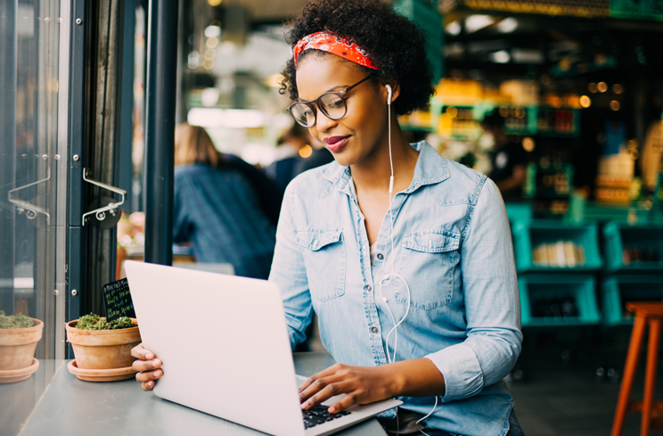 Woman smiles while looking at laptop in a coffee house